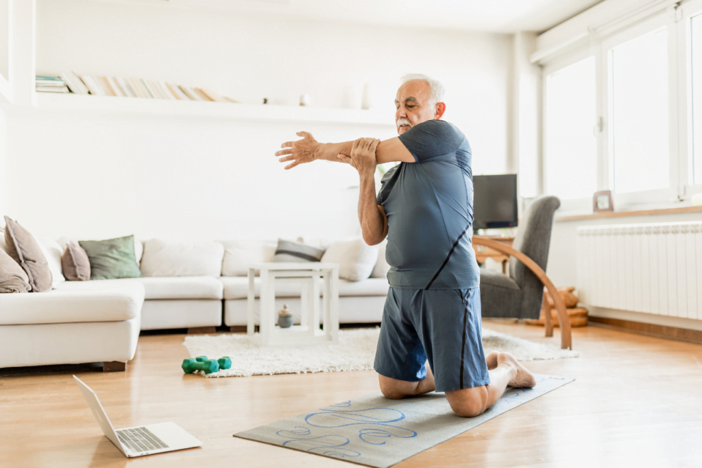 An elderly man doing shoulder stretches during the online fitness classes